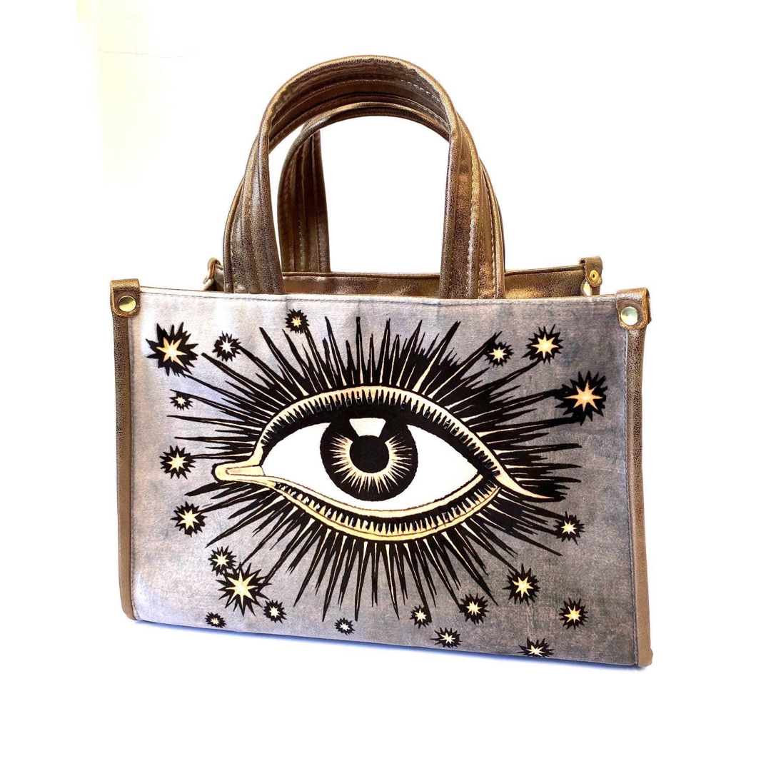 Silver hand bag with an image of an eye with sunbursts and sun rays. Brand: La Funky Mexicana