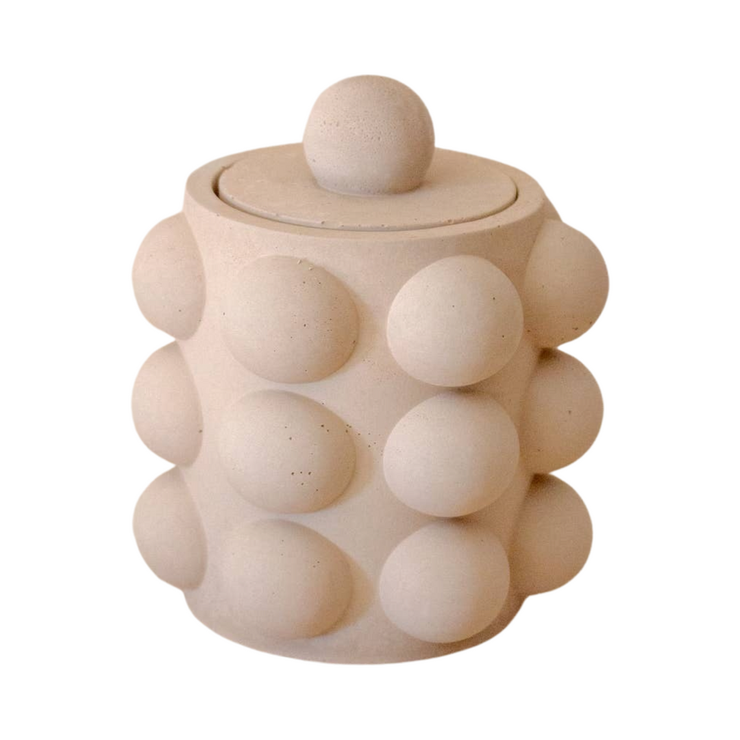 Beige cylinder shaped candle vessel with a bubble texture and a lid.