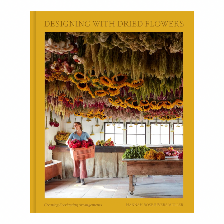 Designing with Dried Flowers book cover by Hannah Rose Rivers Muller, showing a woman holding a basket of flowers beneath a ceiling covered in hanging dried blooms"