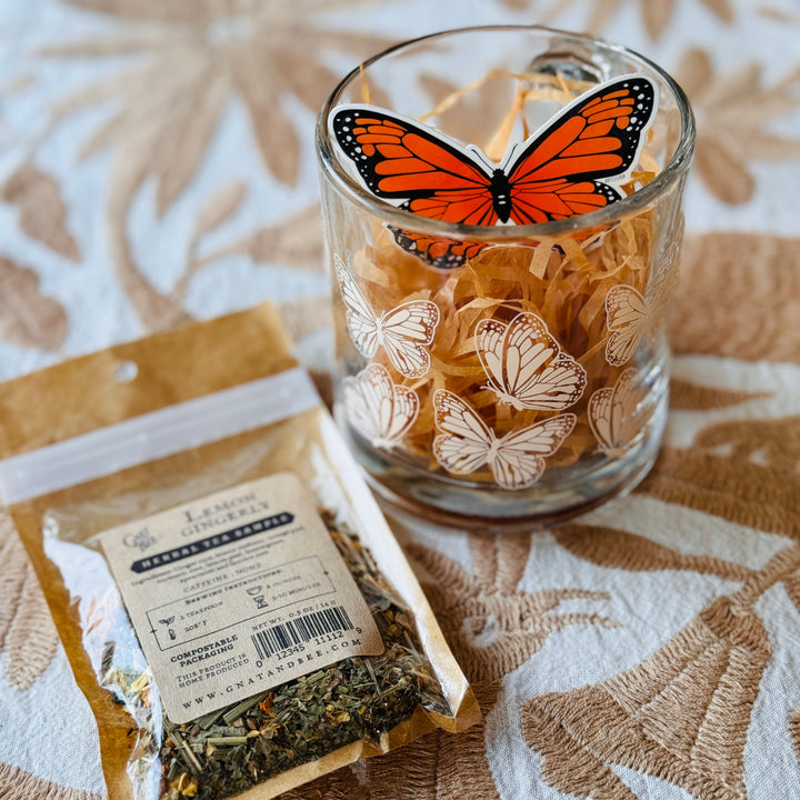 clear mug withe creme colored butterfly graphics, a pack of tea, some Kraft crinkle paper and a monarch butterfly sticker