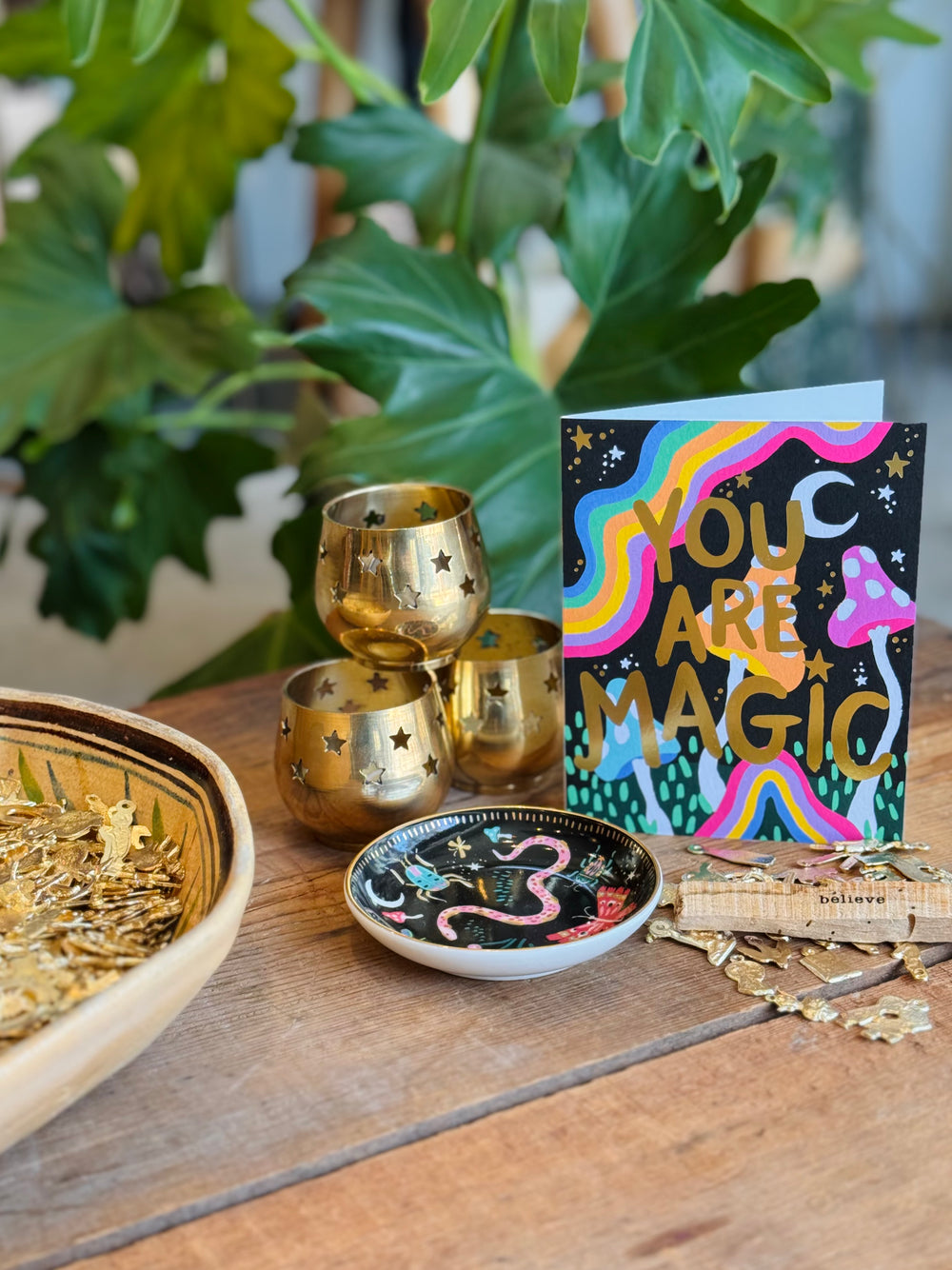 Decorative items including gold tumblers, a bowl with gold stars, and a 'You Are Magic' card on a wooden surface with plants in the background.
