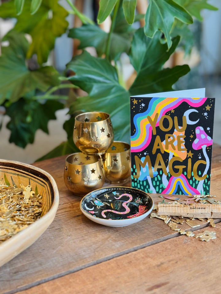 Decorative items including gold tumblers, a bowl with gold stars, and a 'You Are Magic' card on a wooden surface with plants in the background.