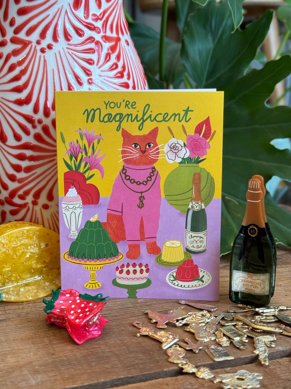 Card with a cat illustration and text 'You're Magnificent' on a table with decorative items.