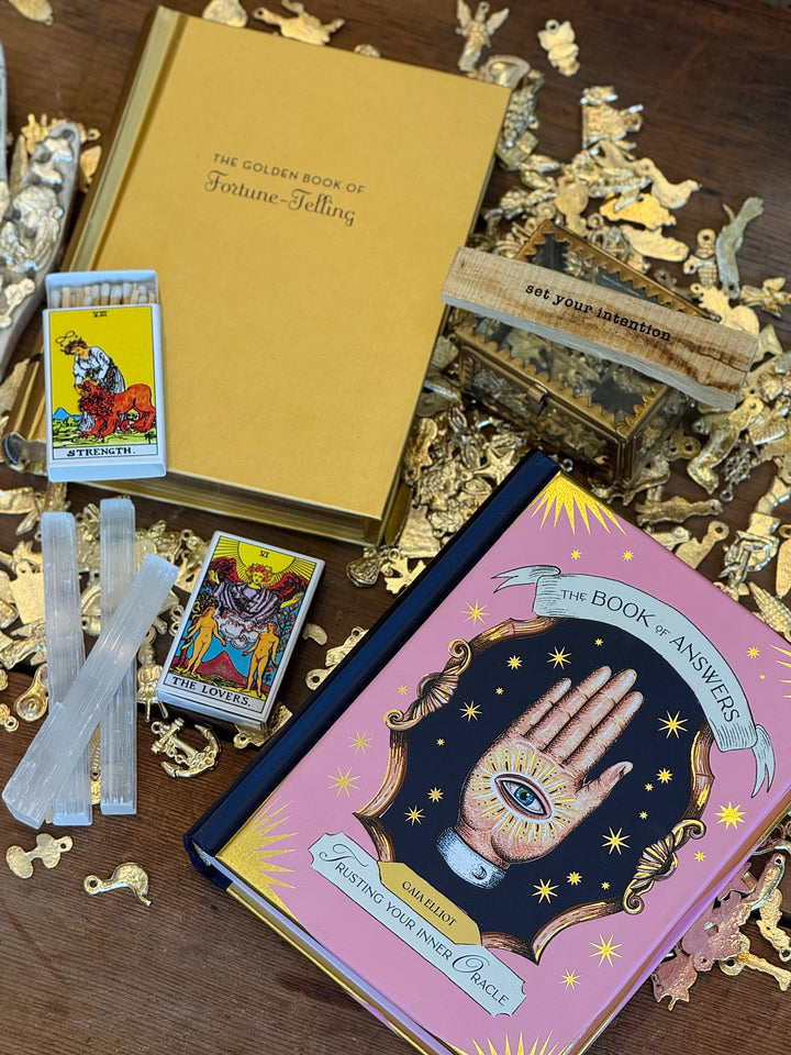 Close up room view displays fortune telling themed books, tarot cards and accessories on a wooden surface.