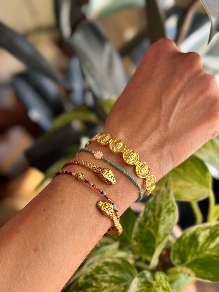 Close-up of a wrist wearing multiple gold and colorful bracelets with a blurred plant background