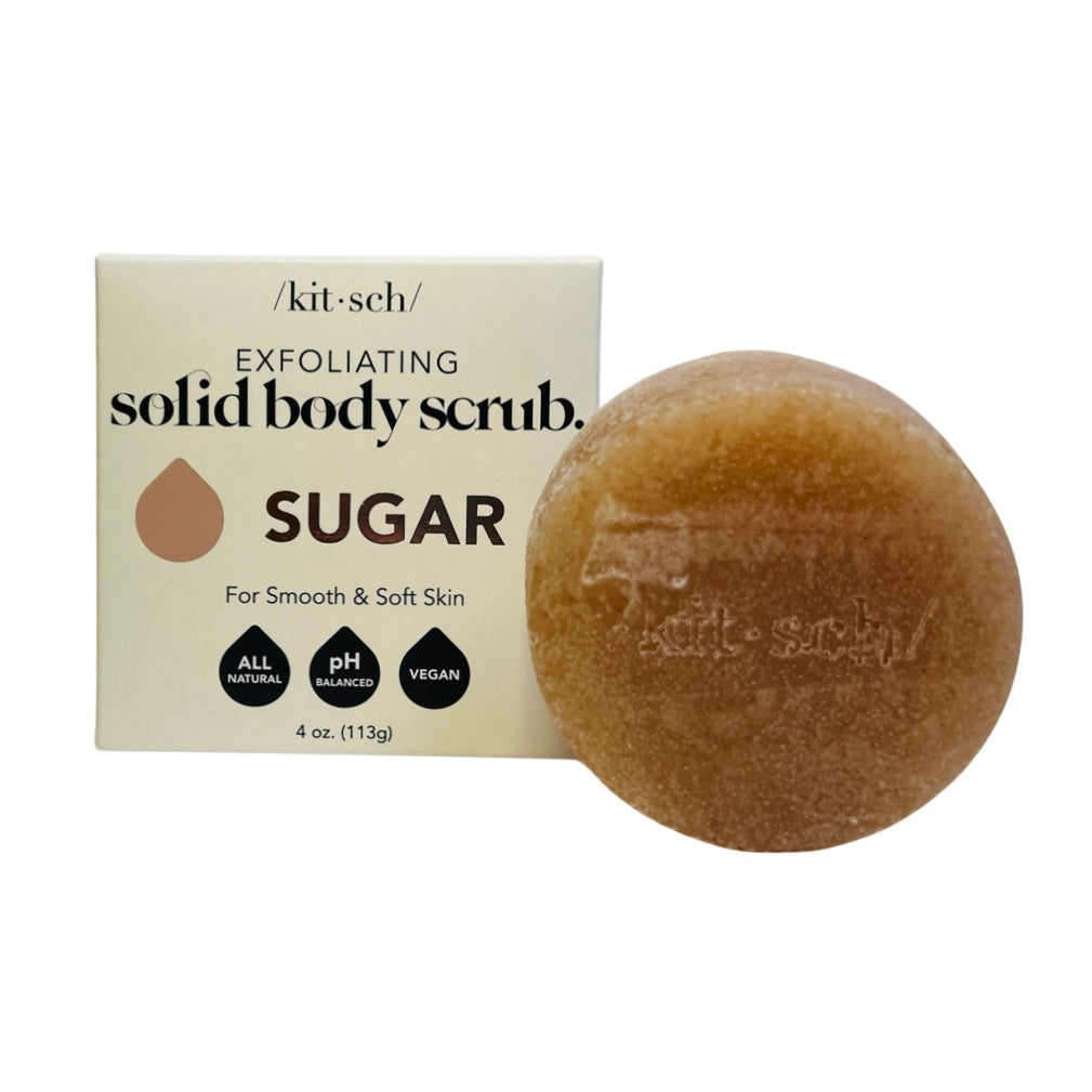 Cream branded box of body sugar scrub and at its side a round bar of body scrub. Brand: Kitsch