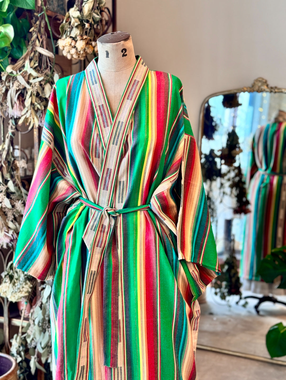 green ikat striped cotton robe on a dress form with a mirror and dried flower bundles in the background