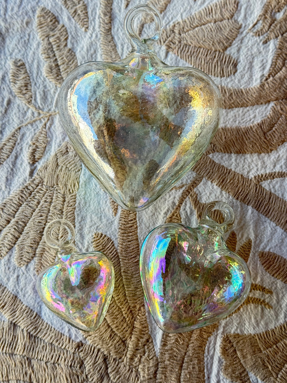 Iridescent heart-shaped glass ornaments on a textured fabric background