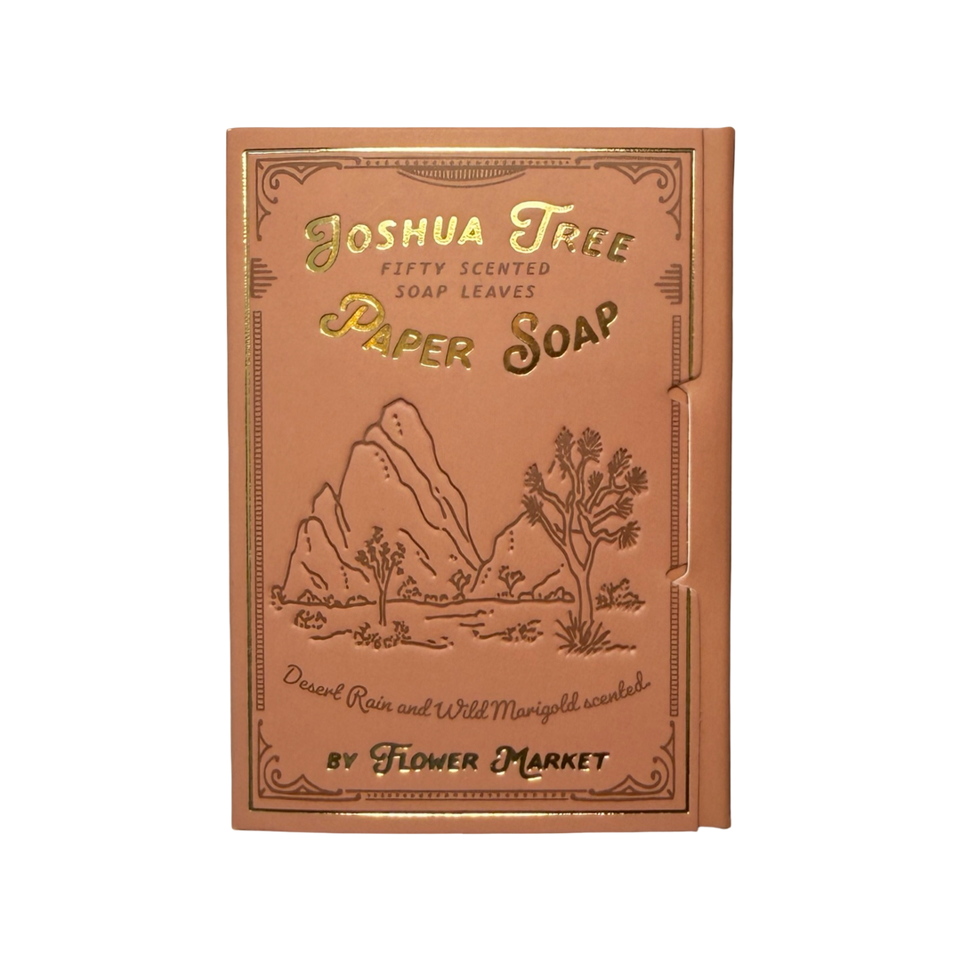 A dusty rose booklet of Flower Market Joshua Tree Paper Soap with gold foil lettering and an embossed desert landscape illustration, fifty scented soap leaves inside.