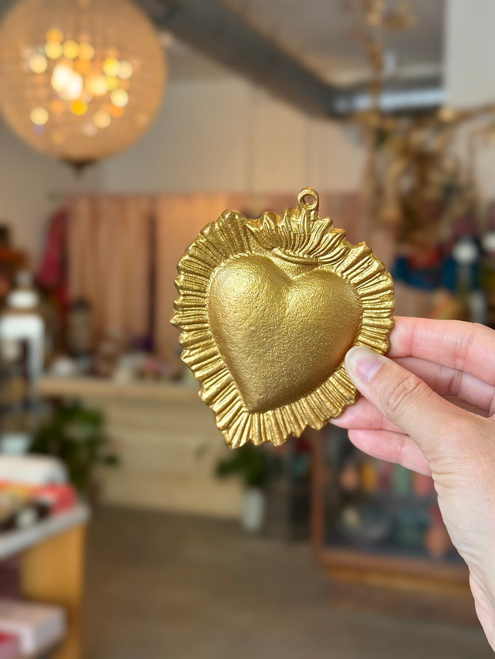 Gold heart-shaped decorative item held in a hand with a blurred indoor background