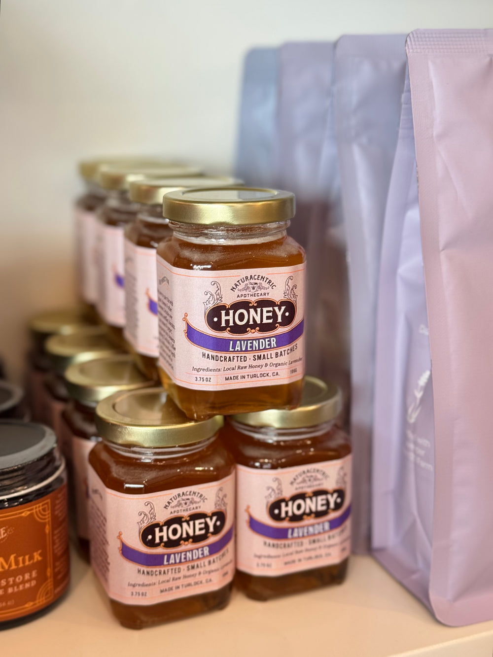 Jars of lavender honey on a shelf with a purple bag in the background.