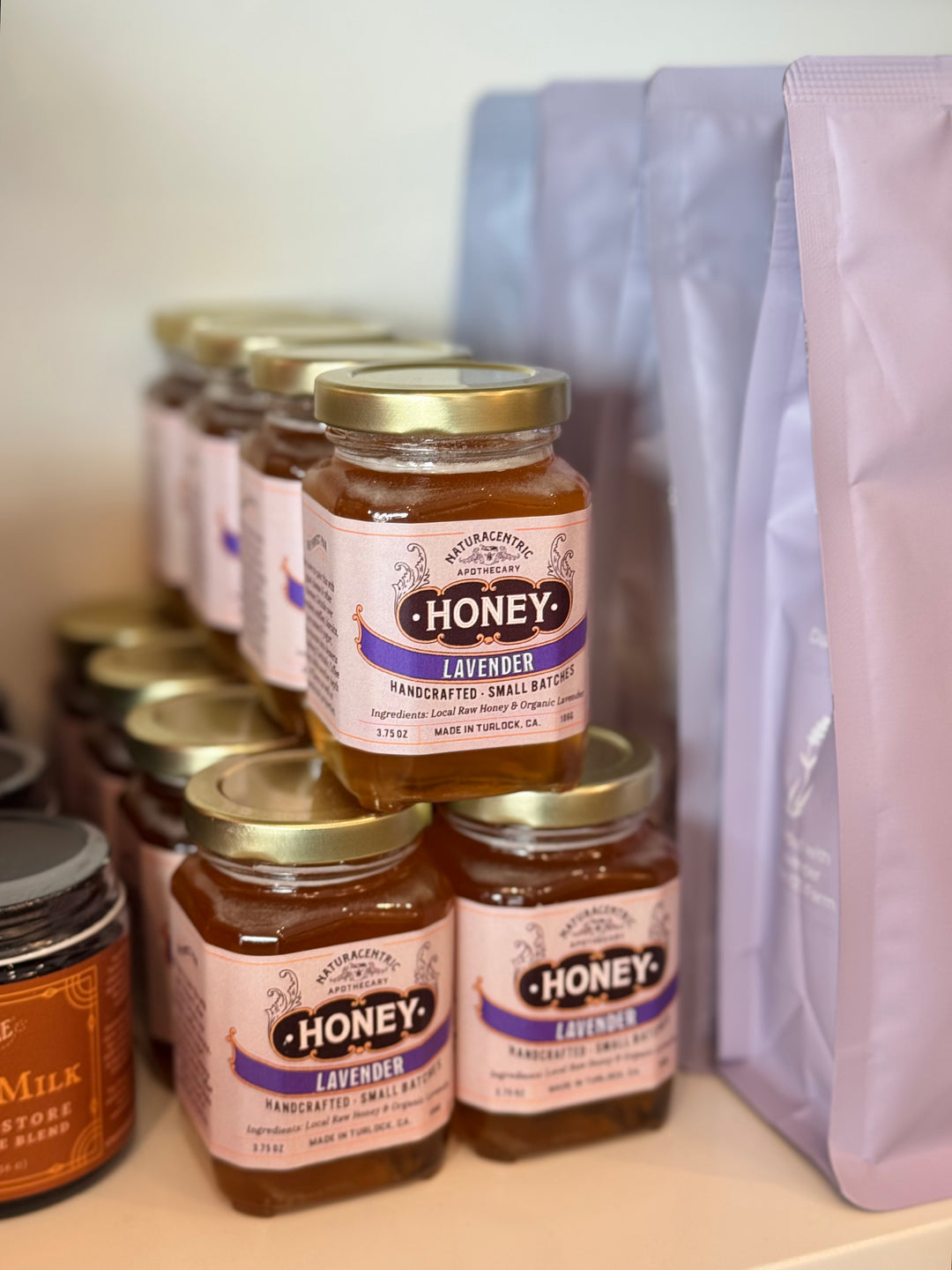 Jars of lavender honey on a shelf with a purple bag in the background.