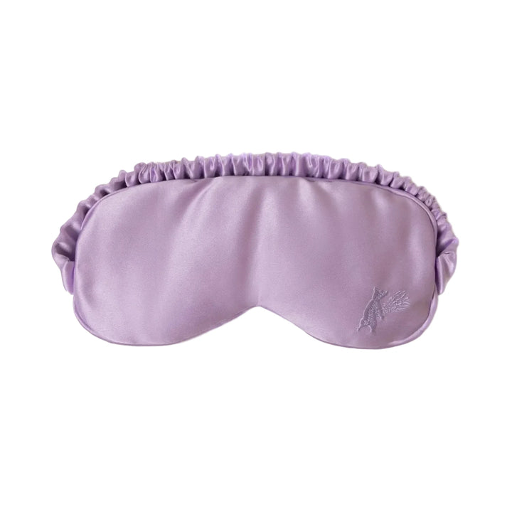 A soft lavender satin sleep eye mask with a ruched elasticated band and a small embroidered floral motif