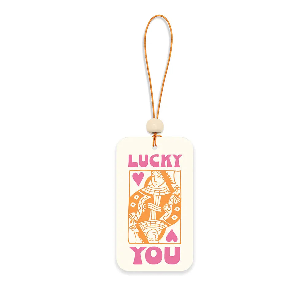 A cream-colored rectangular car air freshener with rounded corners printed with a Queen of Hearts playing card illustration in orange and the words "Lucky You" in hot pink, hanging from a tan cord with a small wooden bead accent.