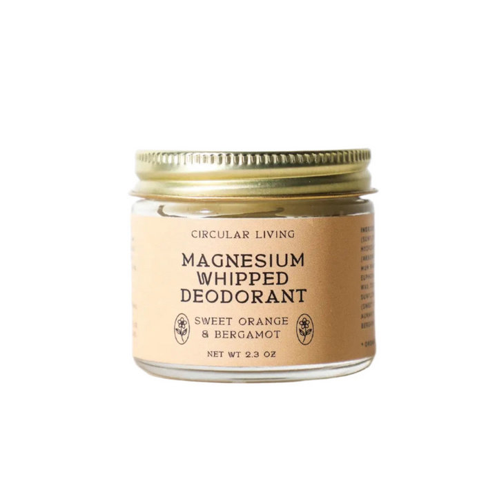 Photo of 2.3 oz clear glass jar with gold lid has beige branded label for Magnesium Whipped Deodorant.