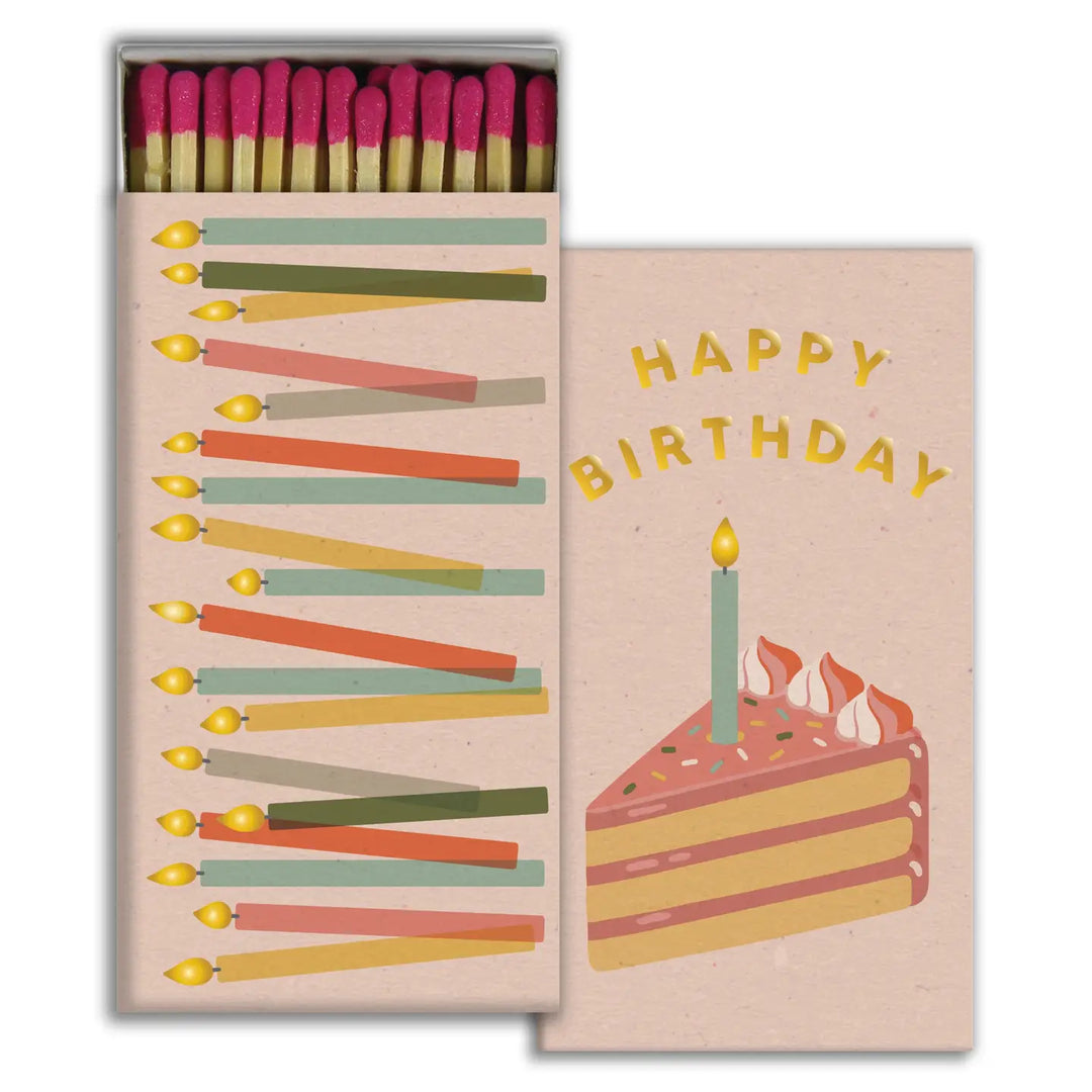 Matchbox with pink-tipped matches, featuring colorful birthday candles on one side and a slice of cake with a single lit candle and the words “Happy Birthday” on the other.