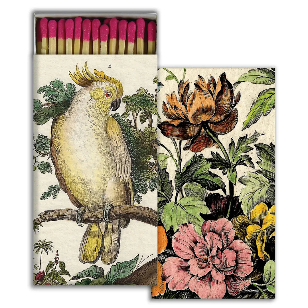 Decorative matchbox with pink-tipped matches, featuring a vintage-style illustration of a cockatoo on one side and colorful botanical flowers on the other.