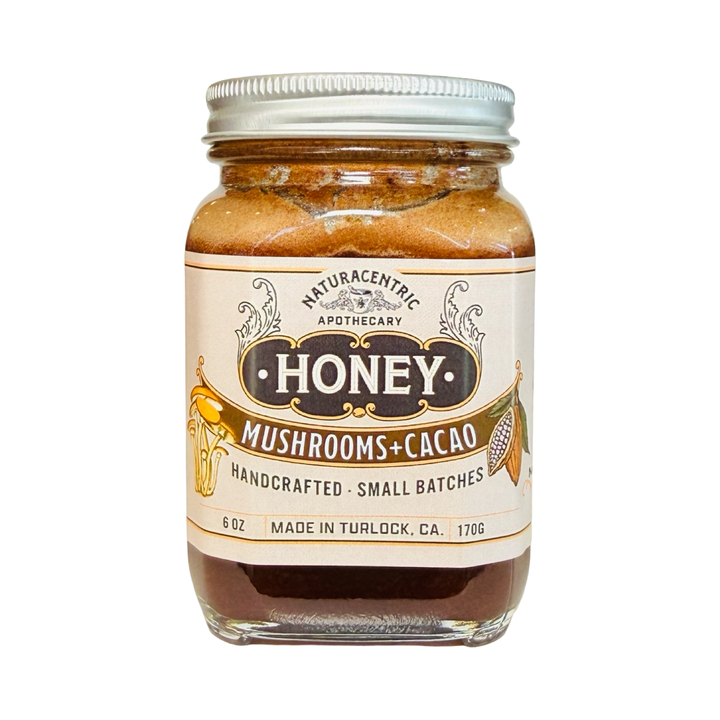 A 6 oz glass jar of Naturacentric Apothecary Mushrooms and Cacao infused honey with a gold lid and vintage-style label