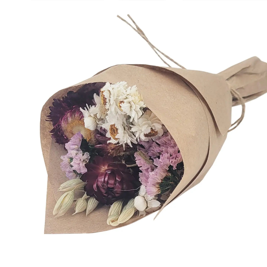 Small dried flower bouquet in purple, white, and burgundy tones wrapped in kraft paper and tied with twine.