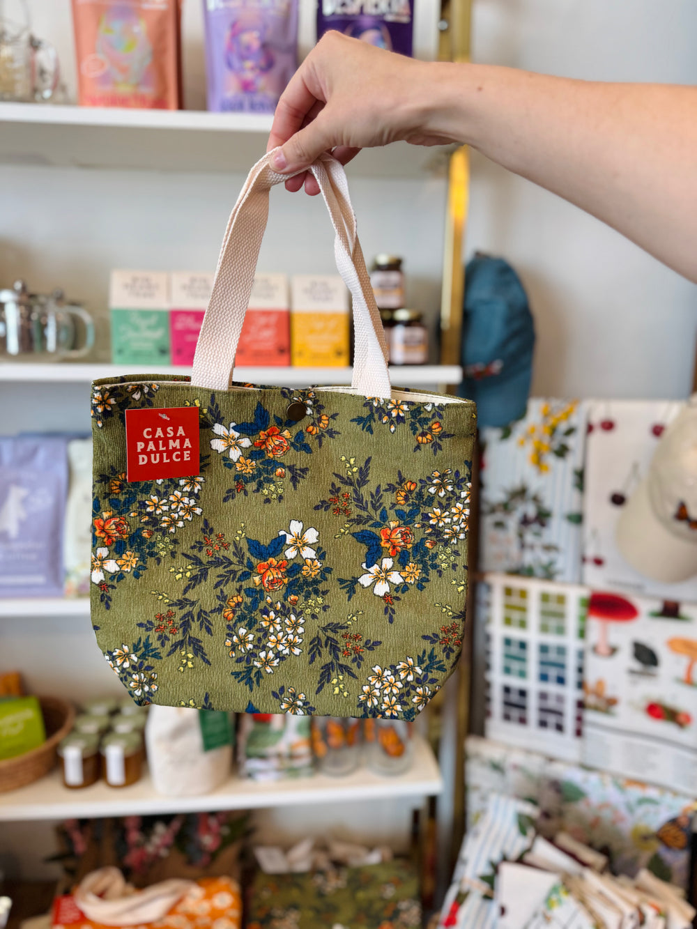 Floral tote bag held by a hand in a store setting