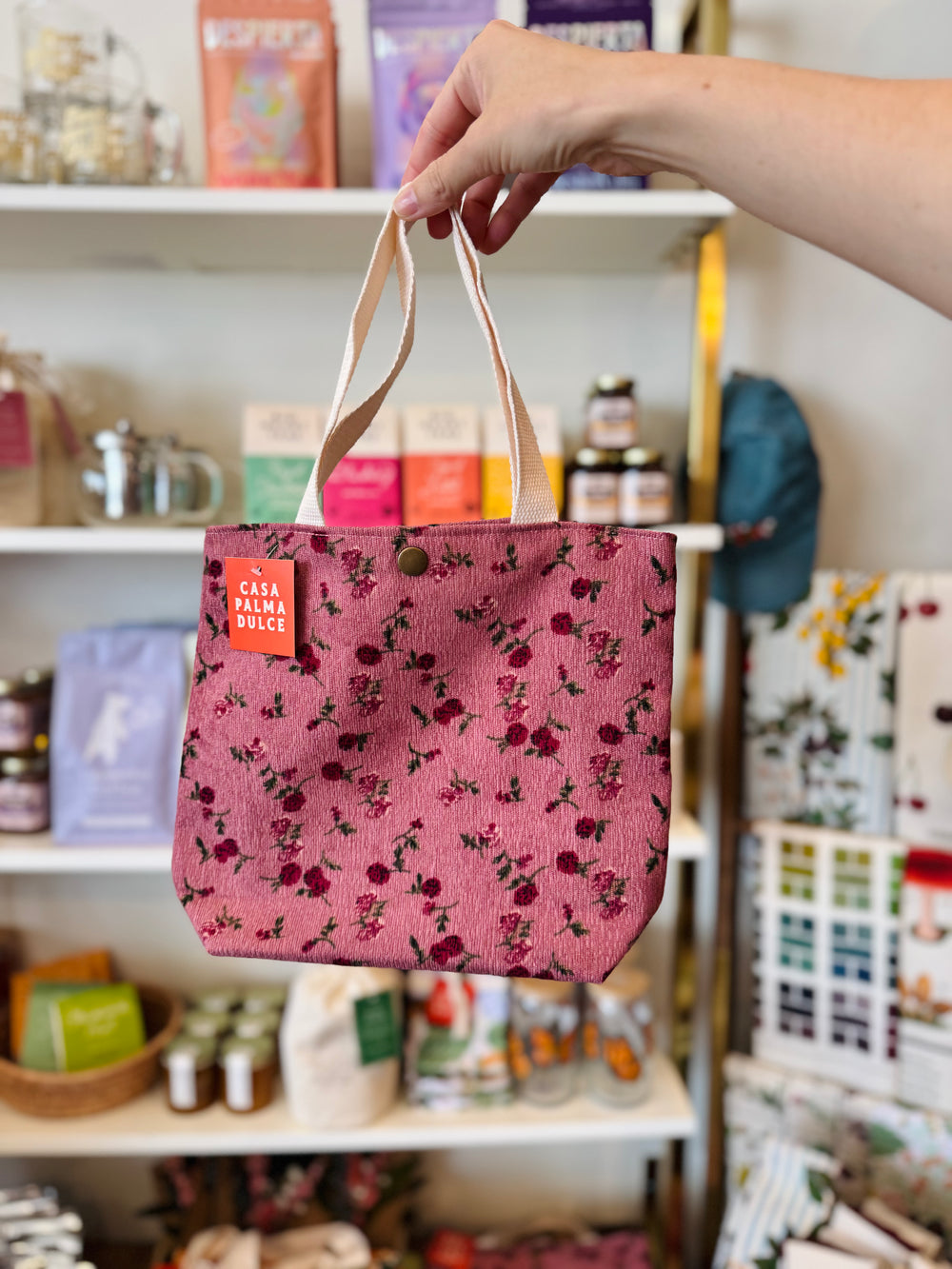 Person holding a pink floral tote bag with a store shelf in the background