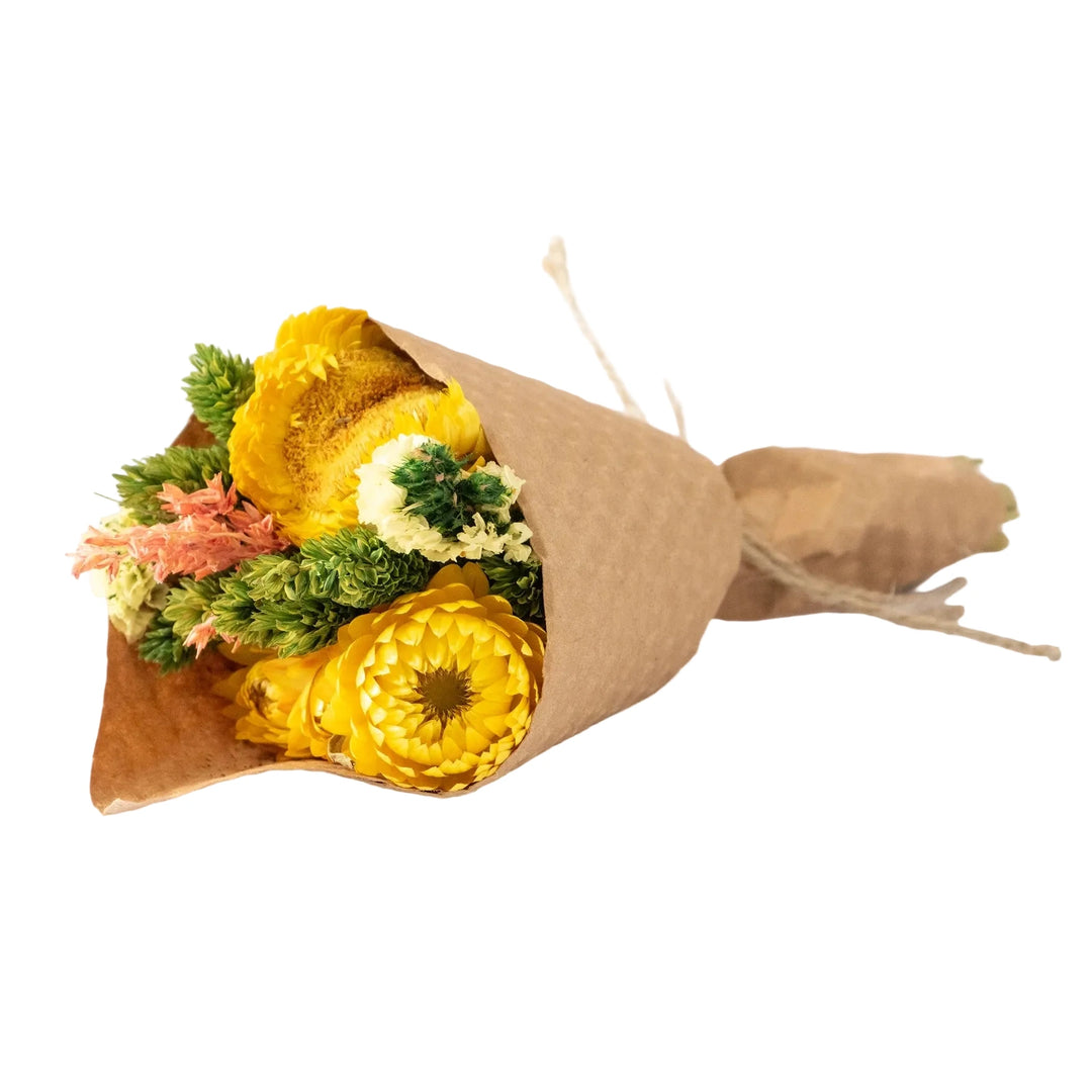 A small dried floral bouquet featuring a central banksia bloom, strawflowers, globe amaranth, and pink filler botanicals, wrapped in a textured cone of kraft paper and tied at the stem with natural twine.