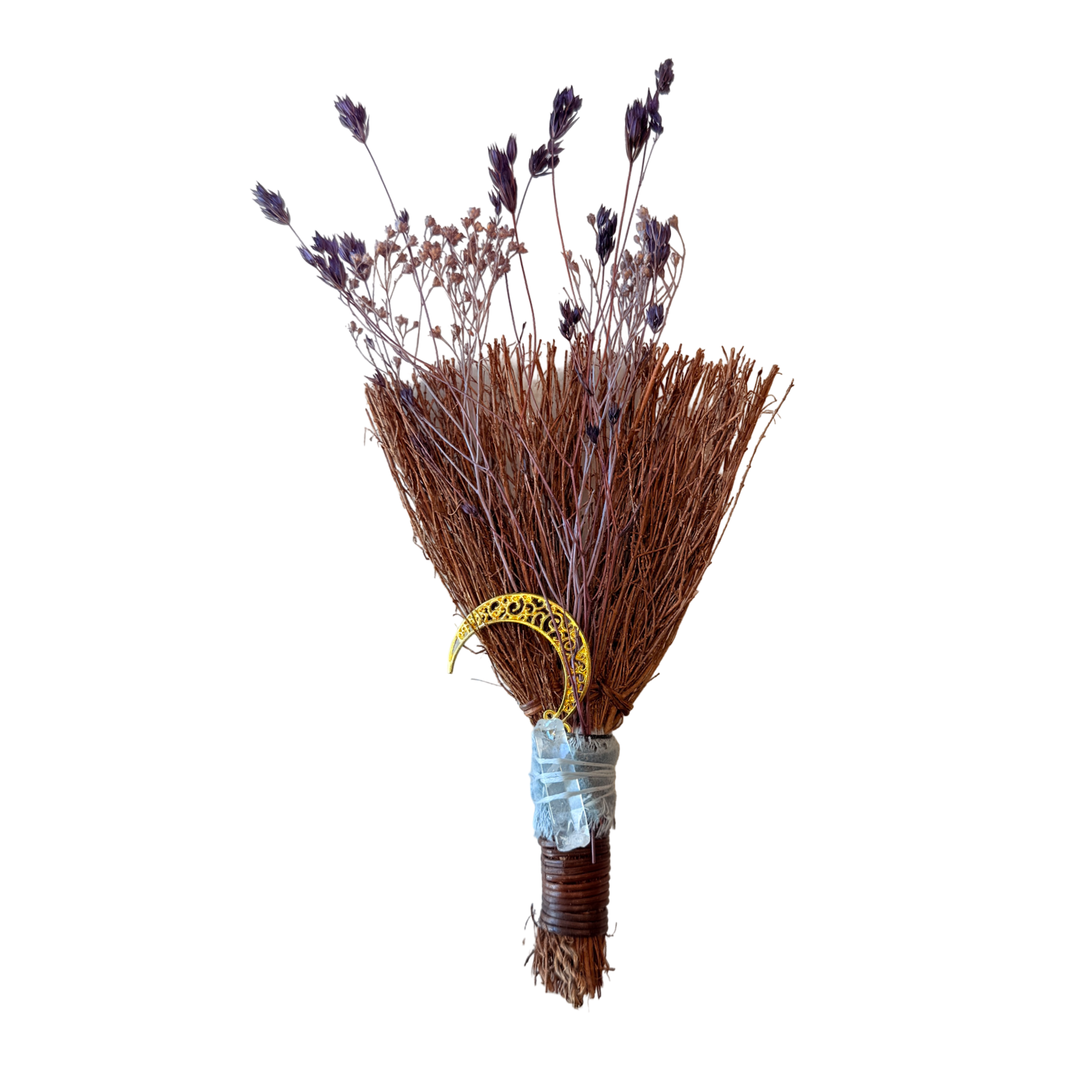 Small handcrafted besom broom made with dried twigs, wrapped in cord, and adorned with a clear quartz crystal and moon charm.