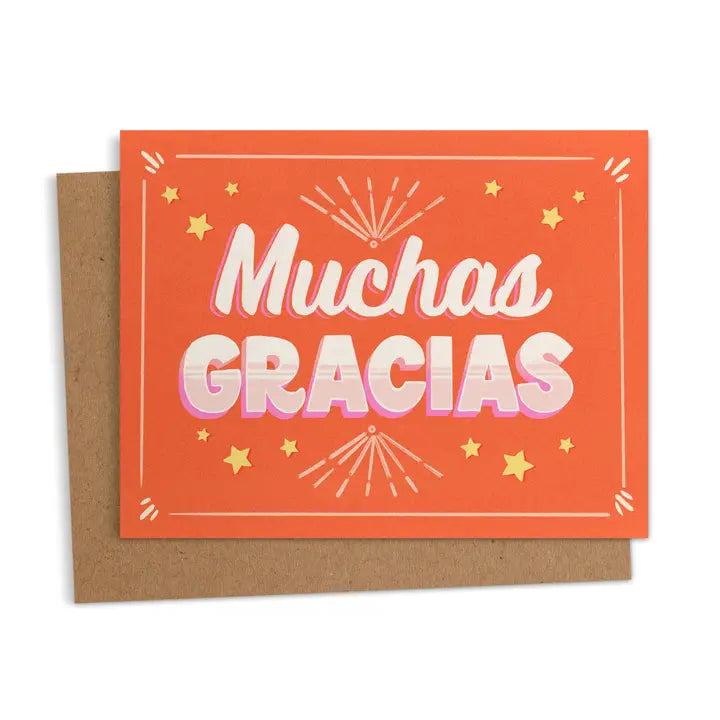 Orange greeting card with the words “Muchas Gracias” in bold white and pink letters, surrounded by stars and decorative bursts is shown in front of a kraft colored envelope.