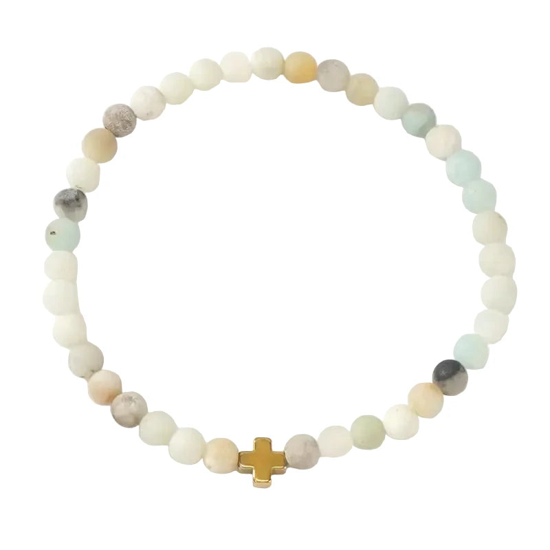 A matte amazonite stretch bracelet in soft cream, white, and sage tones with a small gold cross bead centerpiece.