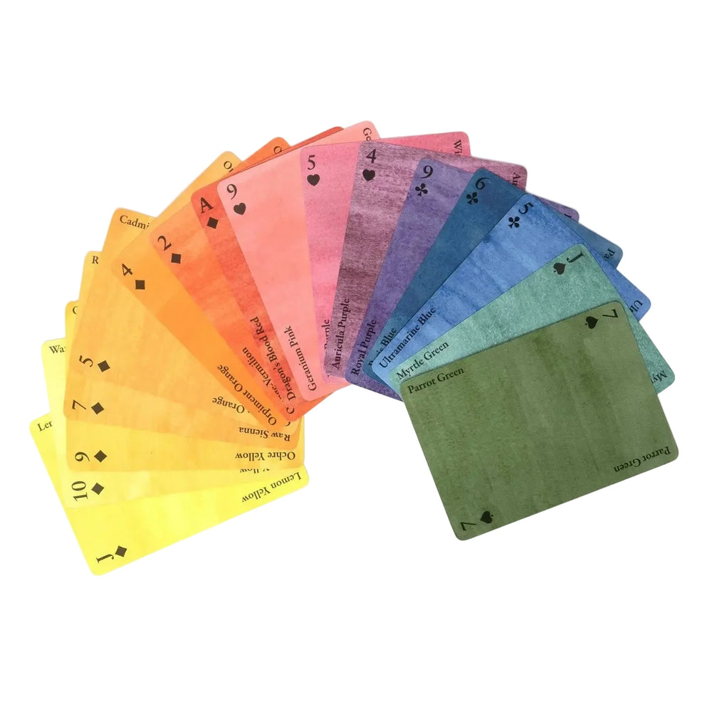 A full fan of Nomenclature of Colors playing cards by Roomytown spread across a white background, each card washed in a different named color spanning the full spectrum from yellow and orange through pink, purple, blue, and green.