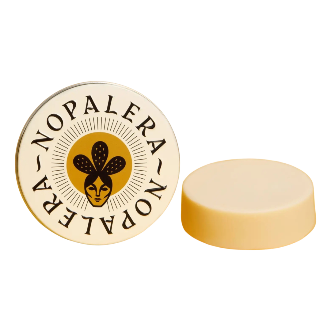 cream round tin featuring an image of a woman wearing a cactus crown and a cream round bar of lotion on the side. Brand: Nopalera