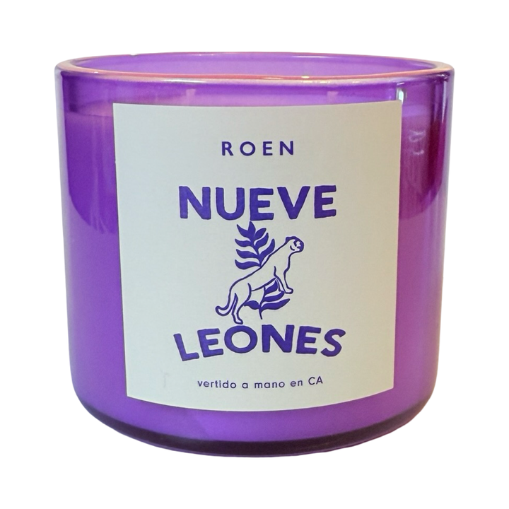 Photo of purple candle jar with branded label that reads "Roen - Nueve Leones - Vertido a mano en CA"