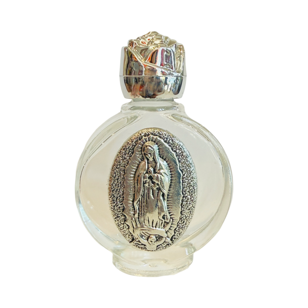 A clear glass bottle with a silver-tone embossed image of Our Lady of Guadalupe on the front. The bottle is topped with a shiny silver cap.