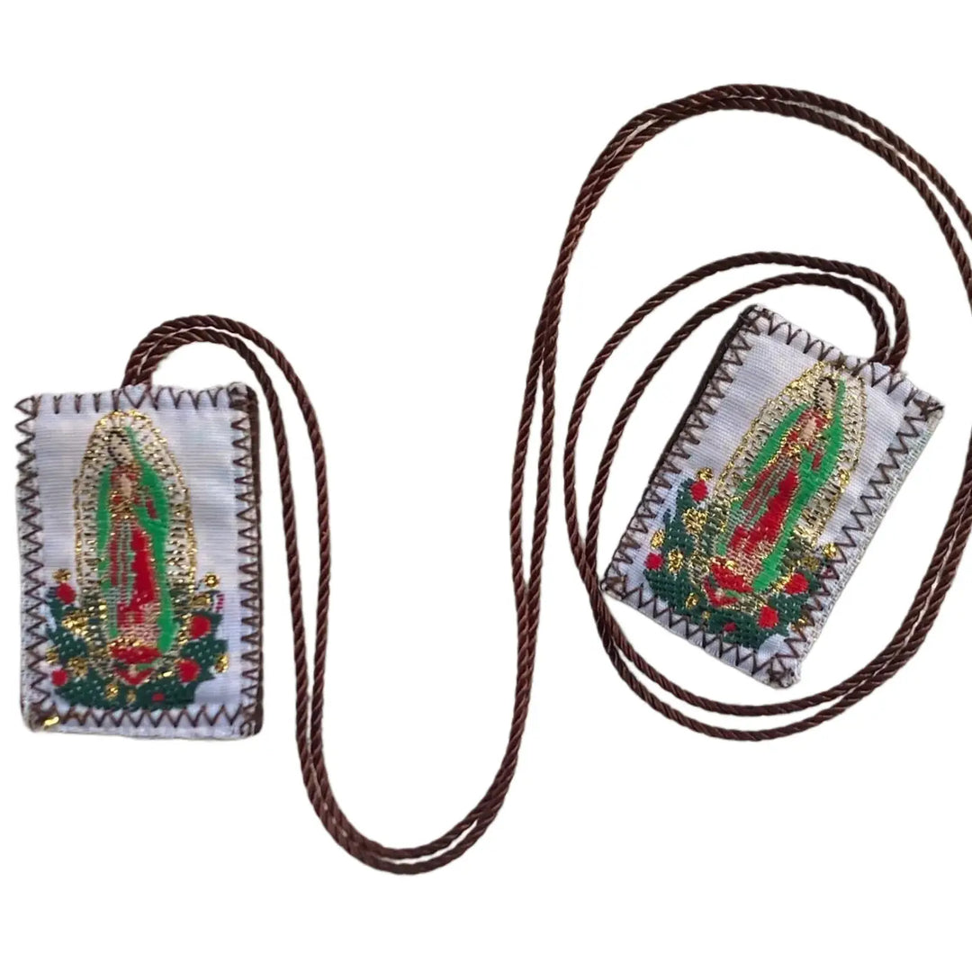 Two small fabric panels joined by a brown cord, each beautifully embroidered with Our Lady of Guadalupe surrounded by floral accents and gold detail.