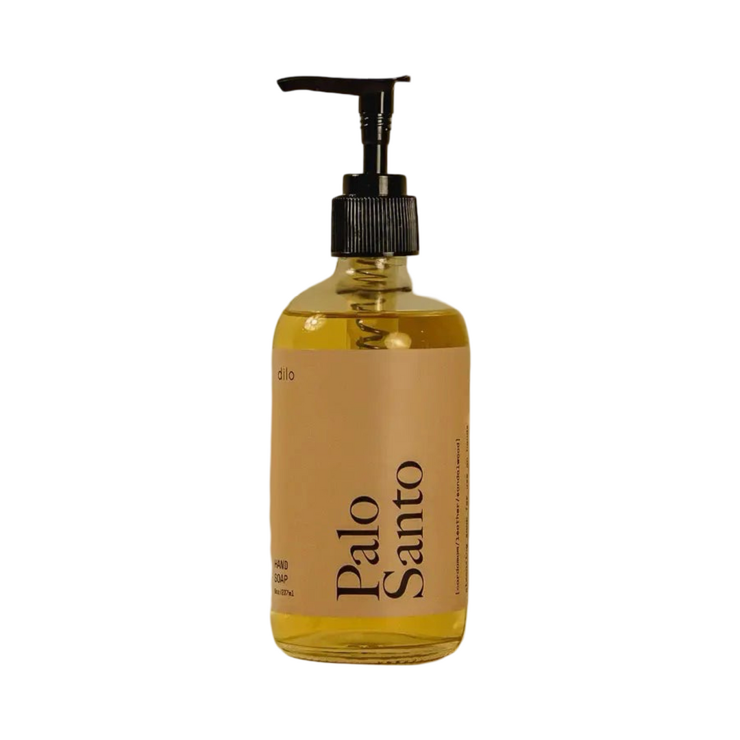 Clear bottle of golden Palo Santo hand soap with branded label and black pump. 