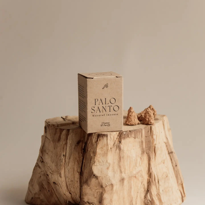 Kraft box of palo santo cones on a wood stump with 3 cones to the right of it.