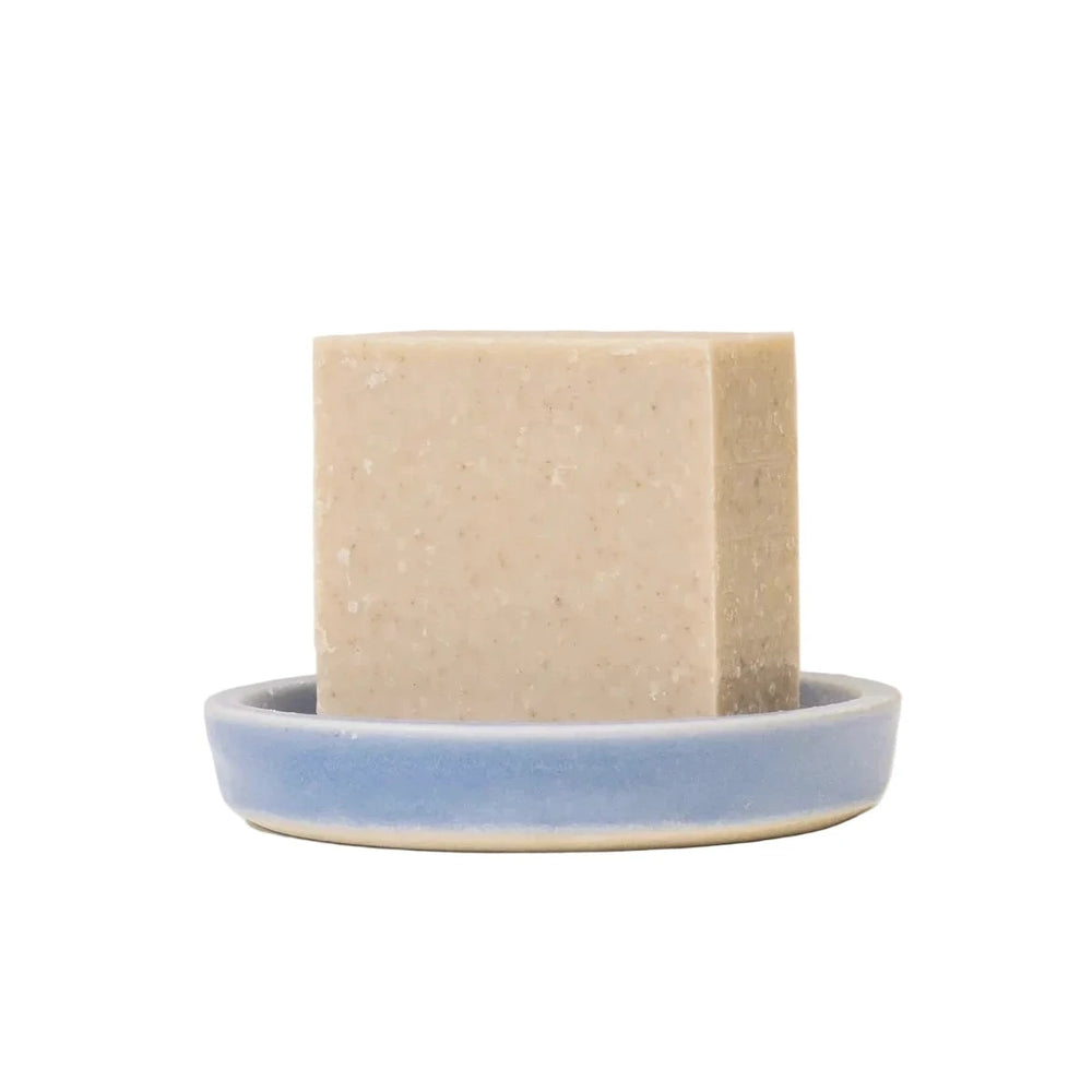 An unwrapped handmade Peppermint and Kelp Body Cleansing Bar resting on a periwinkle blue ceramic soap dish.