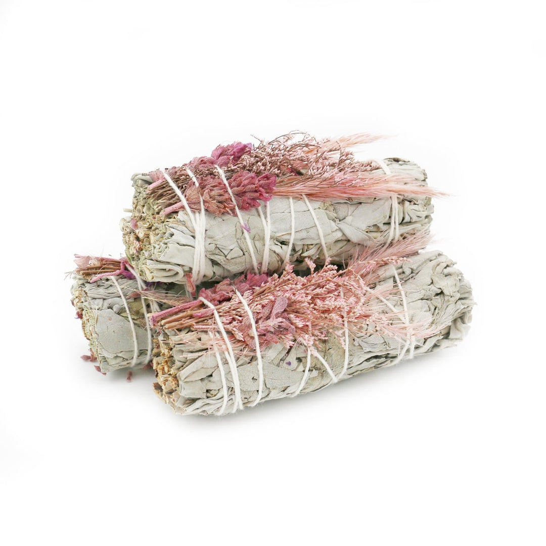 3 sage bundles with light pink colored flowers wrapped in white twine.
