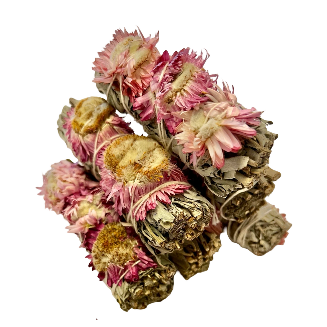 Bundles of white sage wrapped with pink strawflowers and small sunflower-like blooms, tied with white string.