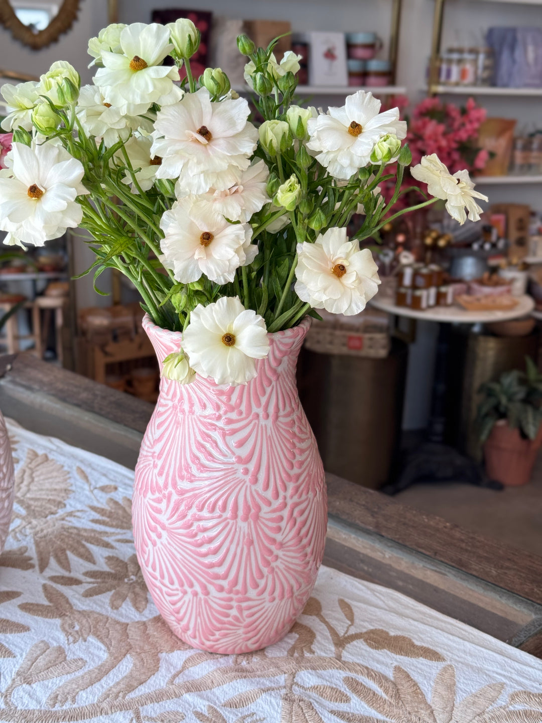 White vase with a pink Puebla design filled with white flowers in a retail background.