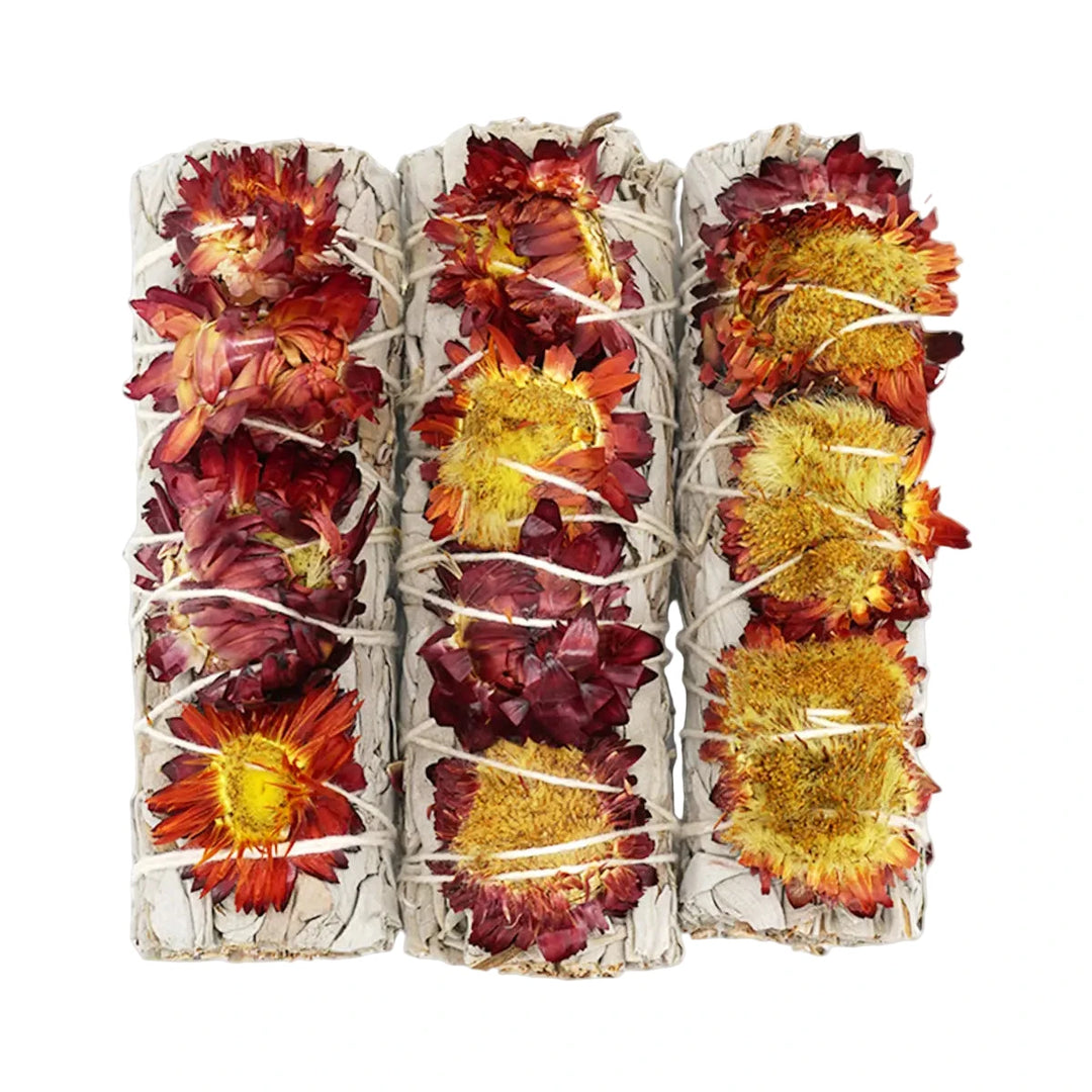 Three white sage bundles wrapped with dried red and yellow sunflowers, tied together with natural string.
