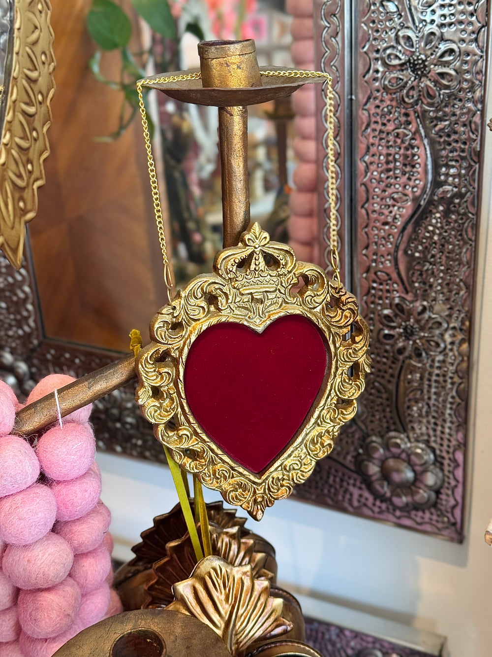 Decorative heart-shaped object with gold frame and red center, held by a chain, against a textured wall.