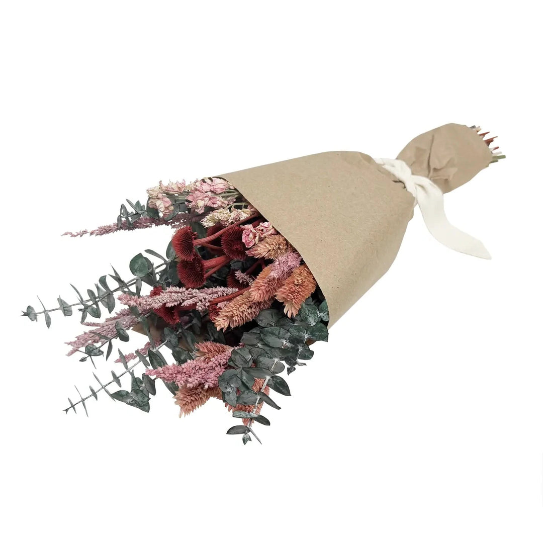 Dried ruby and blush wildflower bouquet wrapped in brown kraft paper and tied with a white ribbon.