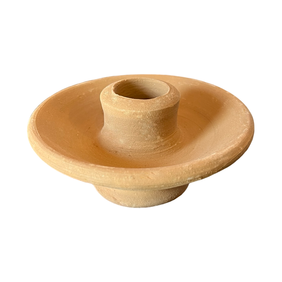 A simple, round, handcrafted terracotta clay candle holder with a central holder for a taper candle and a wide base