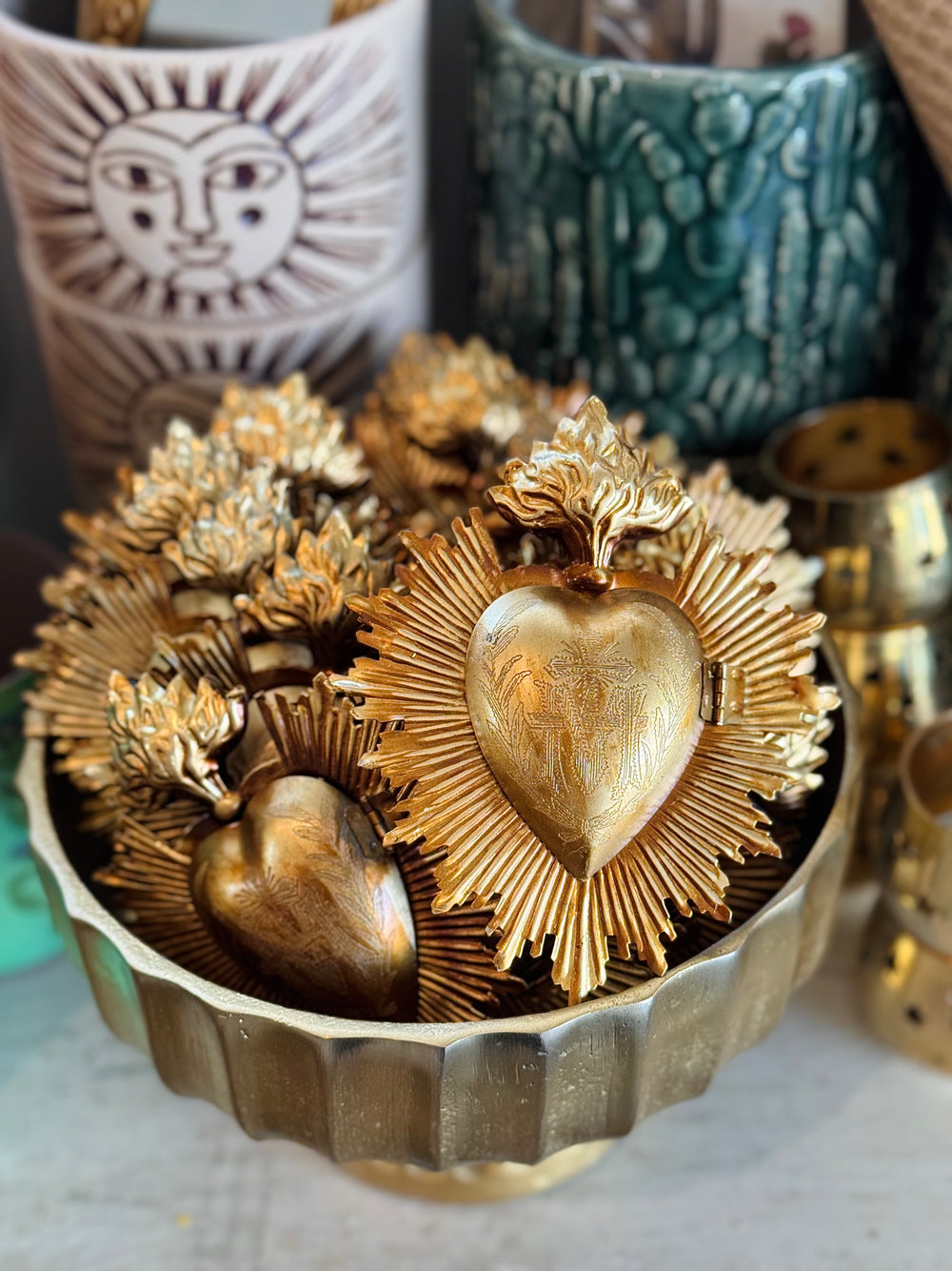 Gold heart-shaped objects in a decorative container with ceramic items in the background
