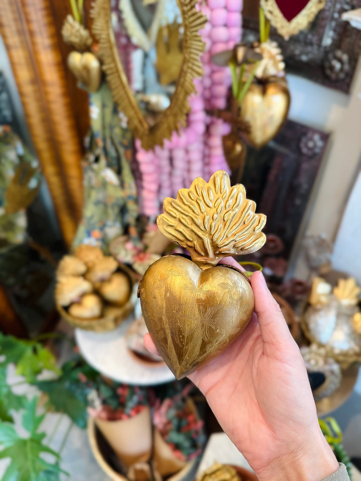 Hand holding a gold heart-shaped object against a decorative background.