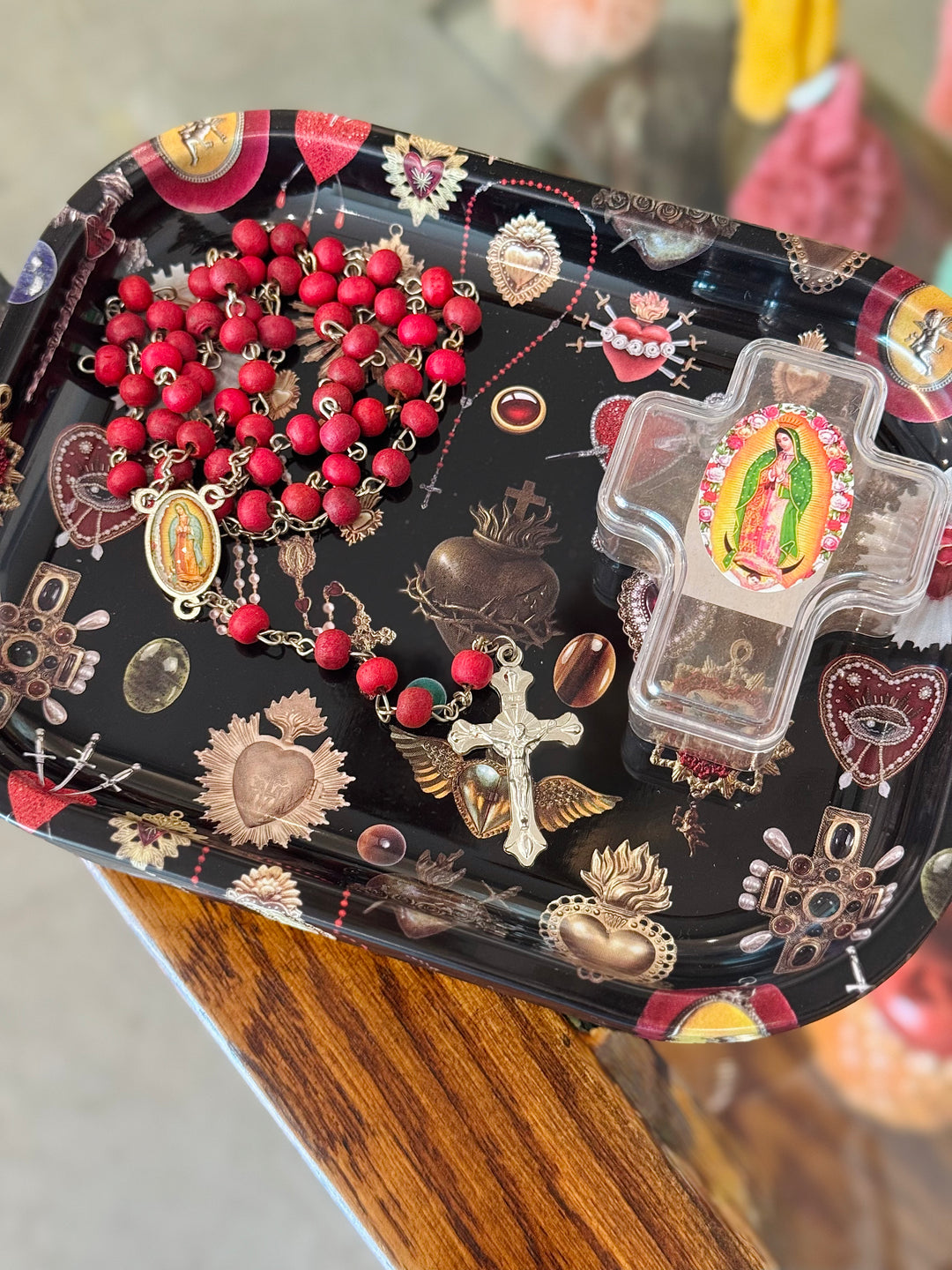 Decorative black tray with religious-themed items including rosaries and crosses on a wooden surface.