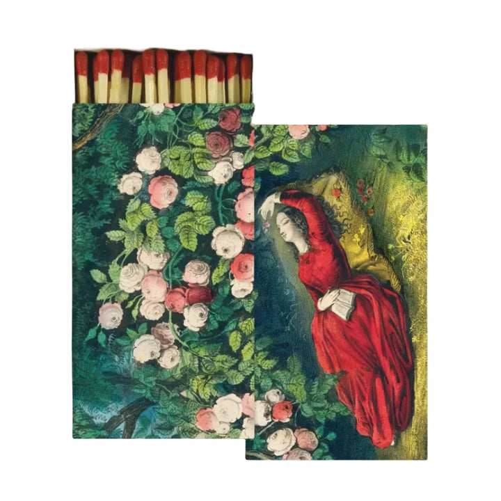 A decorative matchbox featuring a vintage illustration of a woman in red reading among blooming roses, shown open with red tipped matches inside.