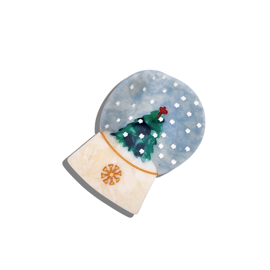 Hand-painted snow globe–shaped hair clip with a Christmas tree inside a snowy blue dome and a pearly white base with a gold snowflake.