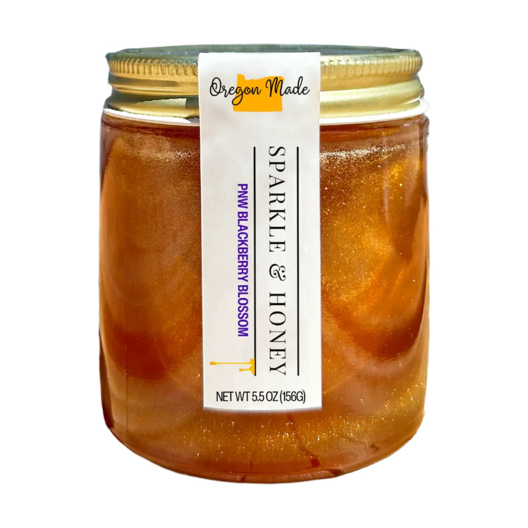 5.5 oz clear jar of golden honey with PNW blackberry blossom mixed with edible glitter has a gold lid with white label.